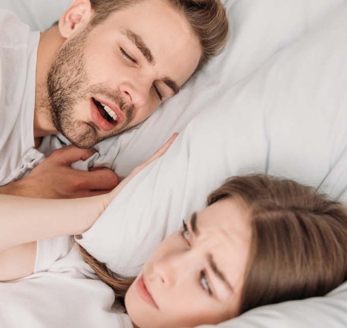 Man snoring in bed next to woman